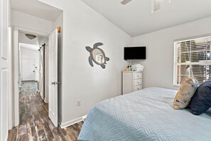 A bedroom with a bed, a television, a wall decoration, and a window with blinds. - The Salty Dog Golf Cart Ocean Lakes (Horry County)
