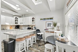 A modern kitchen with white cabinetry, a central island, bar stools, and a dining table. - The Salty Dog Golf Cart Ocean Lakes (Horry County)