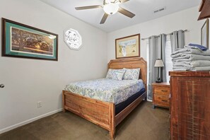 A bedroom with a wooden bed, a nightstand, a dresser, a ceiling fan, and two framed pictures on the wall. - Seas the Day Retreat | GolfCart, LazyRiver & Beach (Horry County)
