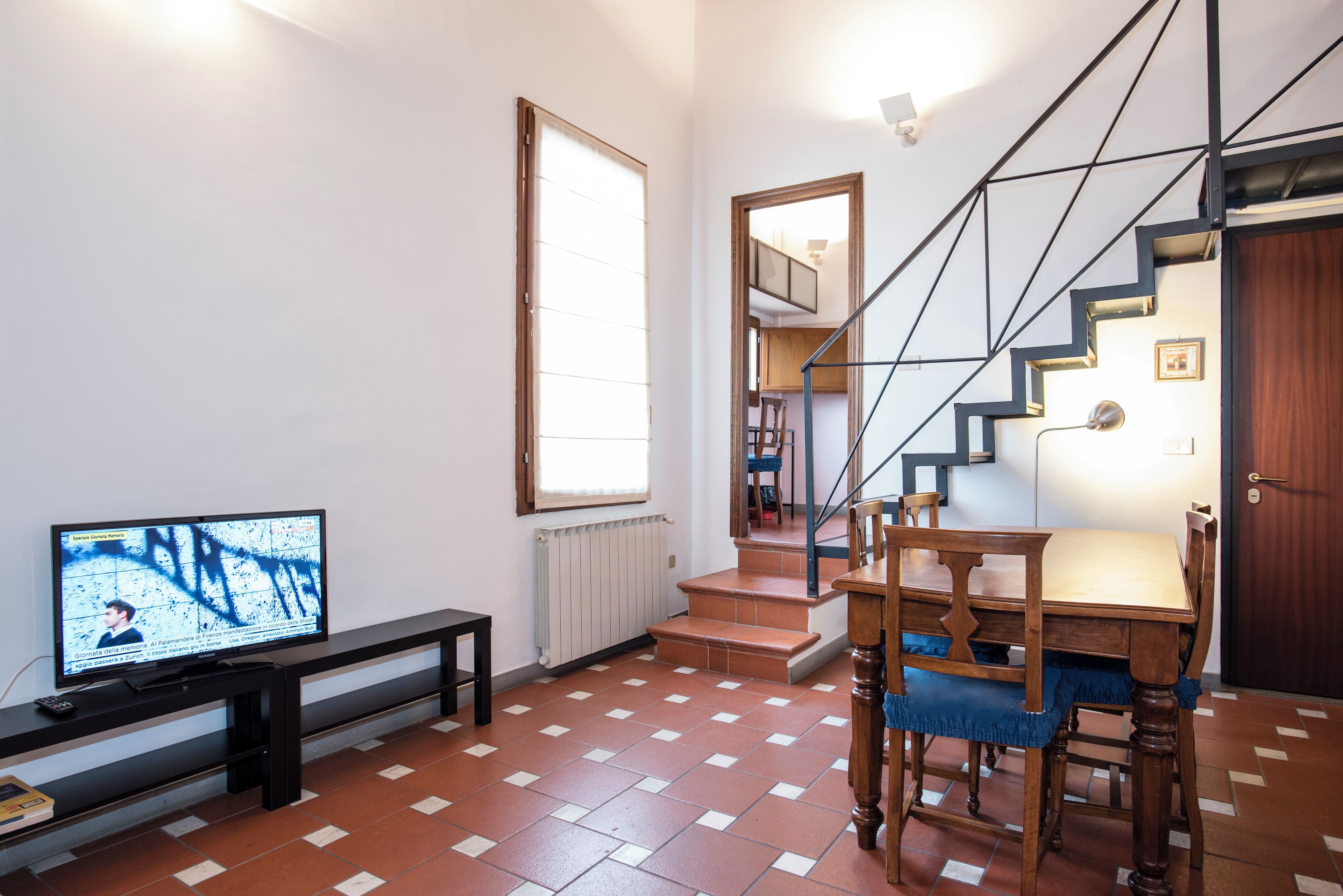 Een moderne woonkamer met een televisie, een bank, een eettafel met stoelen, een trap en een groot raam.