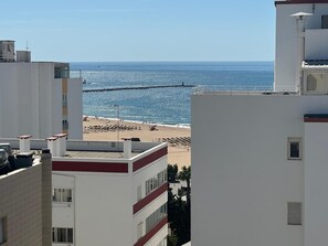 Blick auf die Küste mit Strand und einer Pier, Gebäude im Vordergrund und einem klaren Himmel.