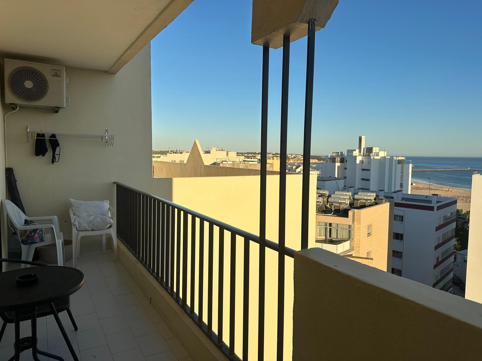 Ein Balkon mit Blick auf das Meer und Gebäude, mit einem Stuhl, einem Tisch und einer Klimaanlage.