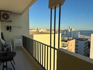 Ein Balkon mit Blick auf das Meer und Gebäude, mit einem Stuhl, einem Tisch und einer Klimaanlage.
