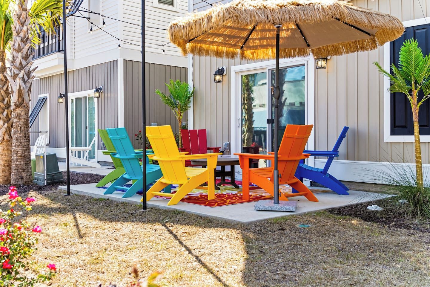 Ein Sitzbereich im Freien mit bunten Adirondack-Stühlen und einem Reetdachschirm.