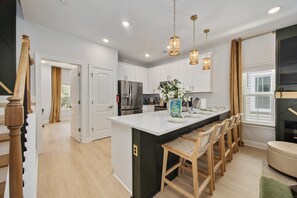 A modern kitchen with a large island, wooden chairs, and pendant lighting. - HGTV-Featured Beach House w/ Glow Arcade (Myrtle Beach)