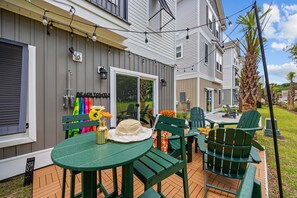 A patio area with green chairs and a table, a sign for 'Beach to Jewels', and string lights. - HGTV-Featured Beach House w/ Glow Arcade (Myrtle Beach)