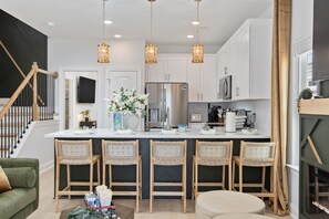 Une cuisine moderne dotée d’un îlot central, d’appareils électroménagers en acier inoxydable et de luminaires suspendus.