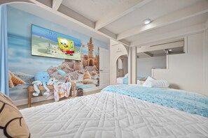 Une chambre à coucher avec un grand lit, un téléviseur diffusant un dessin animé et une fresque murale.