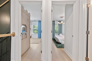 Un pasillo que conduce a un dormitorio con cama, una ventana con cortinas y una puerta con manija.