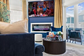 A living room with a large flat-screen TV, a fireplace, a coffee table with snacks, and a comfortable seating area. - Themed Beach House · Private Hot Tub · Neon Arcade (Myrtle Beach)