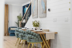 A dining area with a wooden table, teal chairs with gold legs, and a vase with white flowers. - Themed Beach House · Private Hot Tub · Neon Arcade (Myrtle Beach)