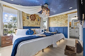 Een slaapkamer met een sterrenhemelplafond, wanddecoratie met een nautisch thema, een bed met blauw beddengoed en een groot raam met uitzicht.