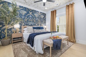 A bedroom with a bed, bedside table, lamp, and a large window with curtains. - Themed Beach House · Private Hot Tub · Neon Arcade (Myrtle Beach)