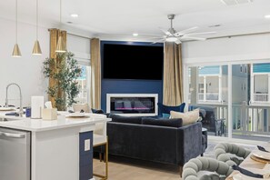 A modern living room with a central seating area, a kitchen island, and a large window with curtains. - Themed Beach House · Private Hot Tub · Neon Arcade (Myrtle Beach)
