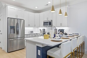 A modern kitchen with white cabinetry, stainless steel appliances, and a central island with seating. - Themed Beach House · Private Hot Tub · Neon Arcade (Myrtle Beach)