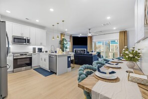 Een moderne keuken met witte kasten, roestvrijstalen apparatuur en een eethoek met een houten tafel en blauwe stoelen.