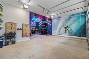 Ein Zimmer mit einer großen Wandmalerei eines Surfers, einem Neonzeichen und Spielautomaten.