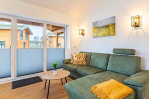 A modern living room with a green sofa, a small round table, and a painting on the wall. - Ferienhaus mit Eigener Sauna und Schoener Terrasse (Toenning)