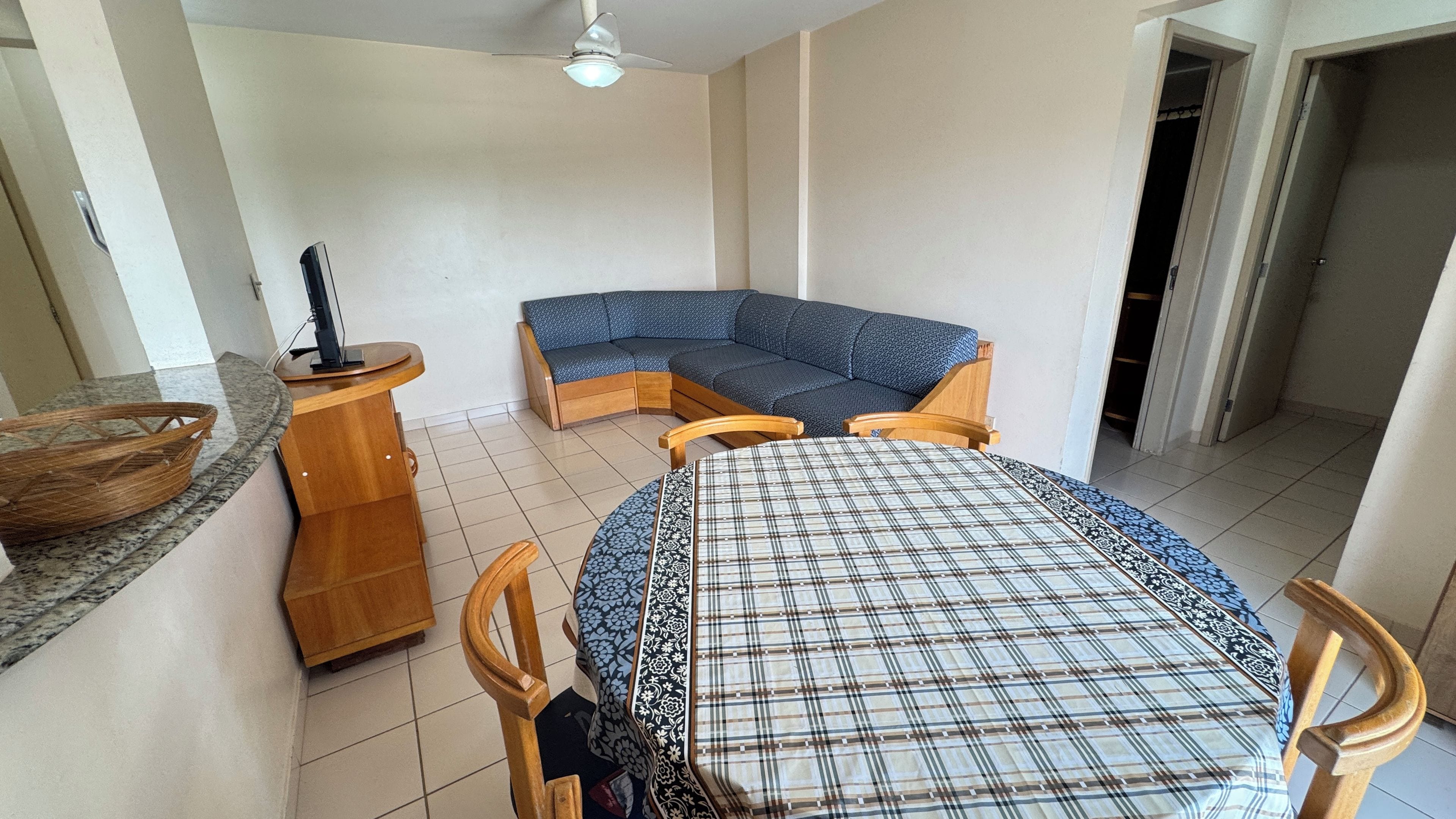 A room with a dining table, a corner sofa, a wooden side table, and a ceiling fan.