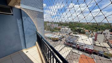 Um edifício alto com fachada azul, uma varanda com guarda-corrimão preto e vista para um horizonte urbano com diversos edifícios e céu claro.