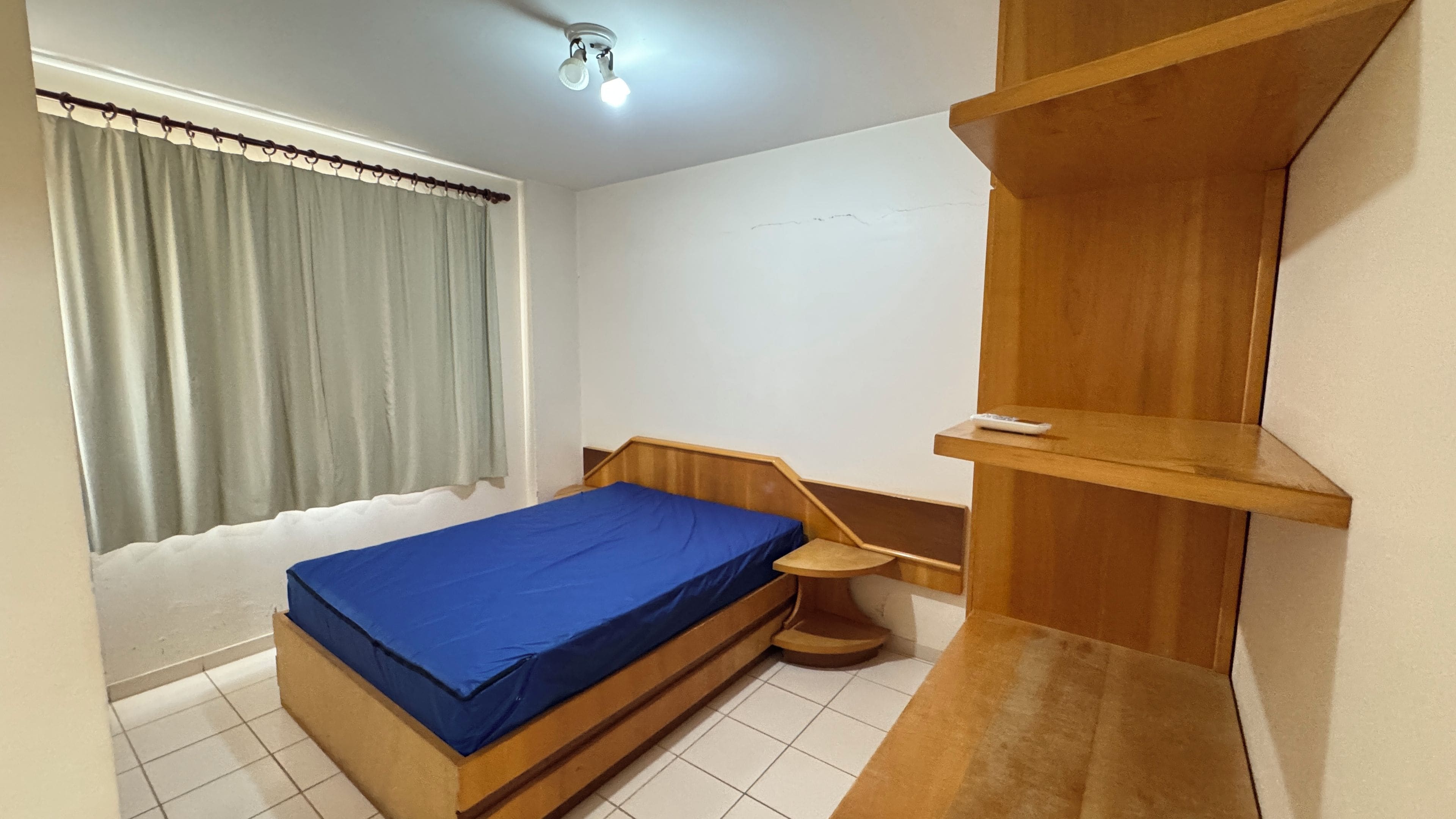 A bedroom with a bed, a wooden shelf, a ceiling fan, and a window with curtains.