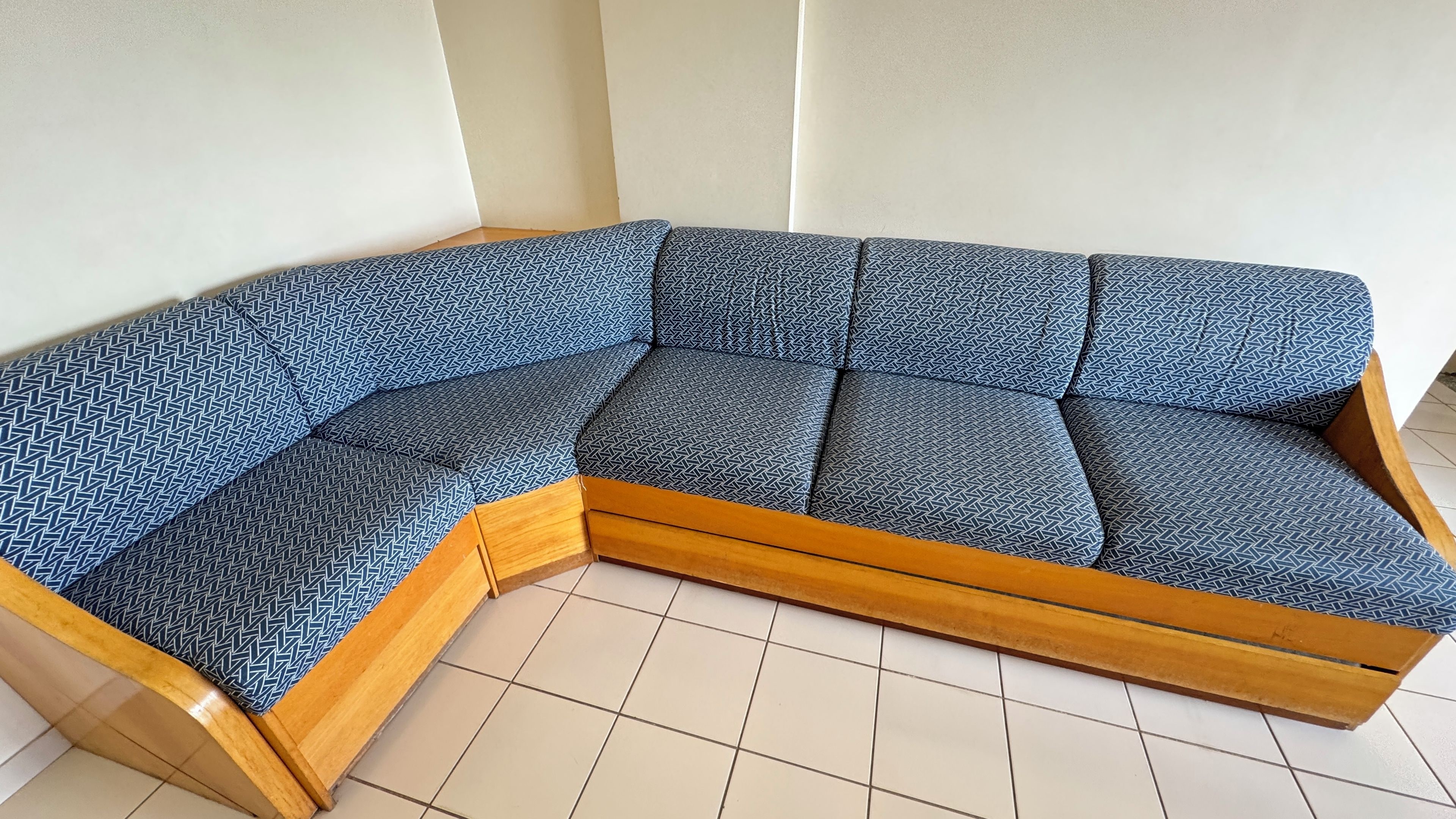 A corner sectional sofa with a geometric pattern, wooden frame, and a tiled floor.