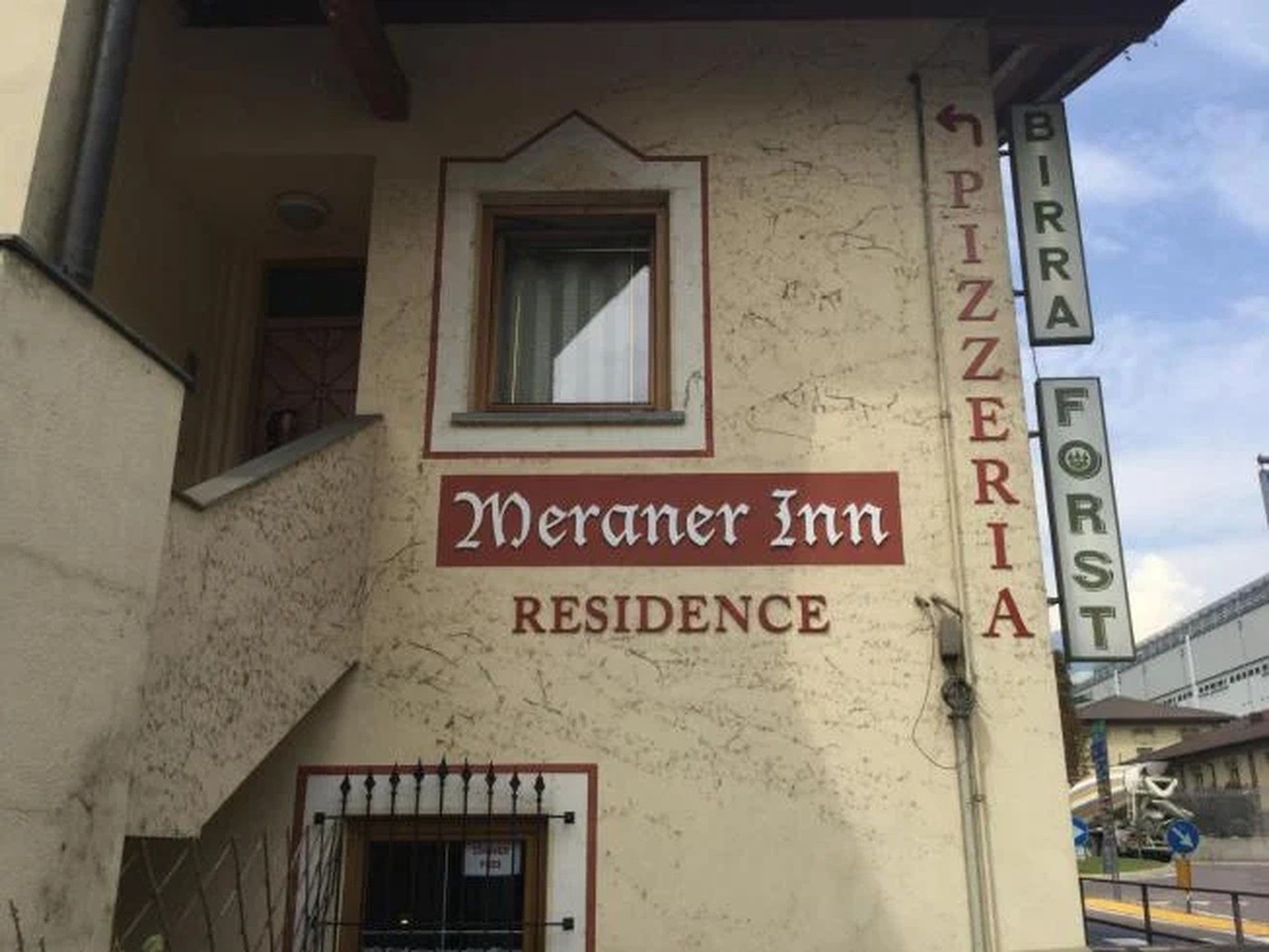 A building with a sign that reads 'Meraner Inn Residence' and 'PIZZERIA' indicating a pizzeria on the side.