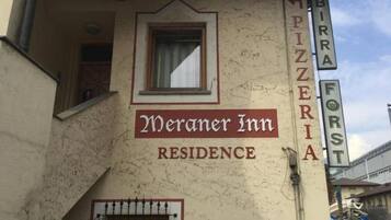 A building with a sign that reads 'Meraner Inn Residence' and 'PIZZERIA' indicating a pizzeria on the side.