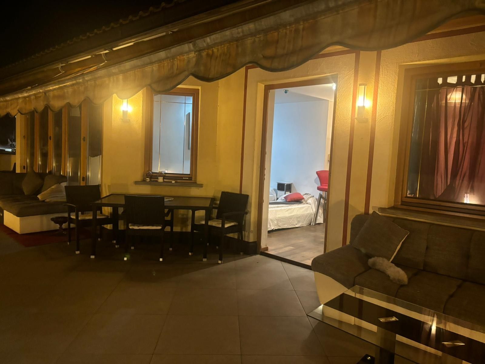 A hotel room with a sofa, a dining table, chairs, a bed, and a window with curtains.