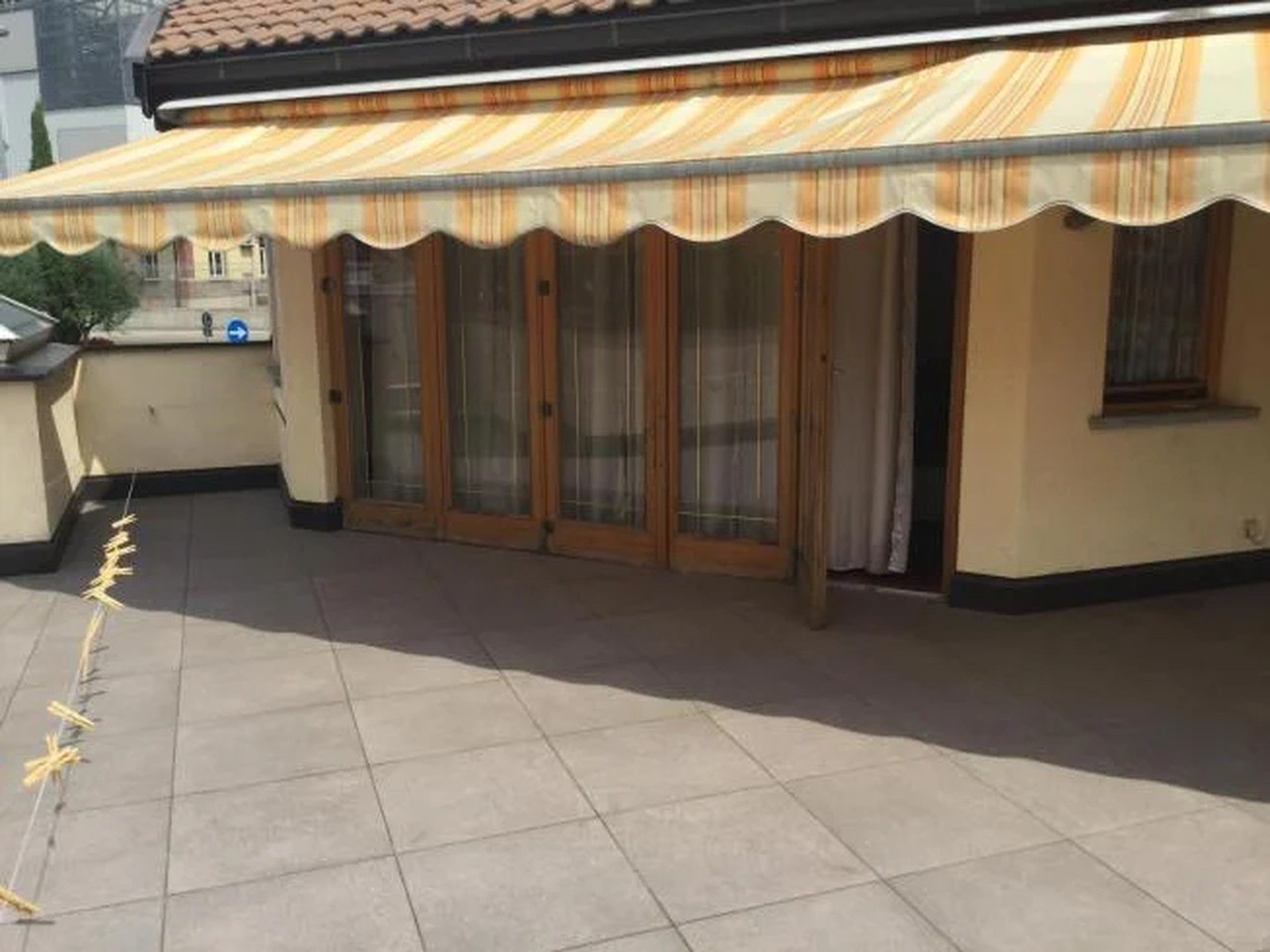 A covered outdoor area with a tiled floor, a wooden door, and a glass door.