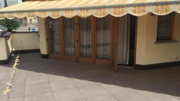 A covered outdoor area with a tiled floor, a wooden door, and a glass door.