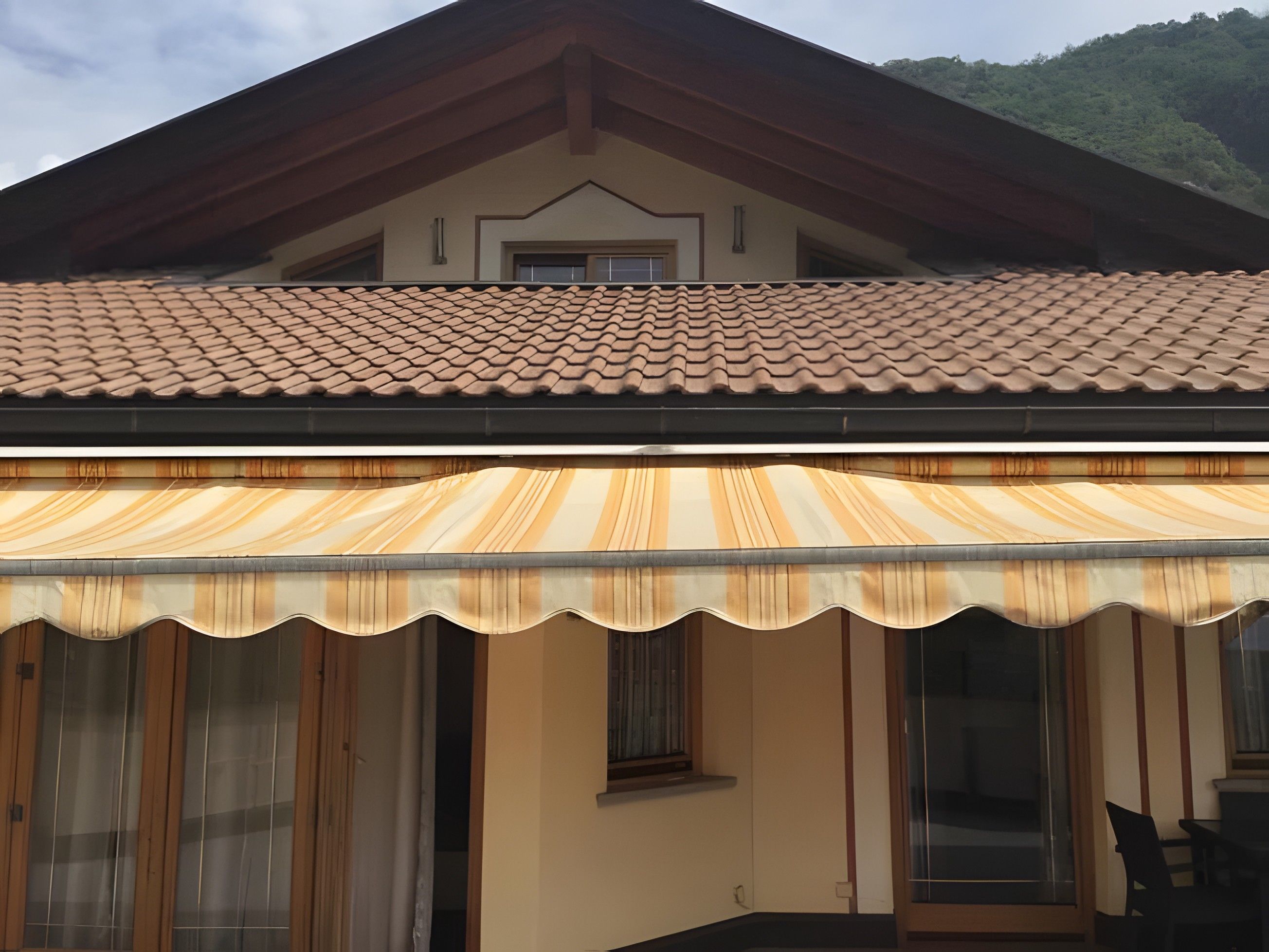 A building with a tiled roof, a covered patio area with a striped awning, and a window.
