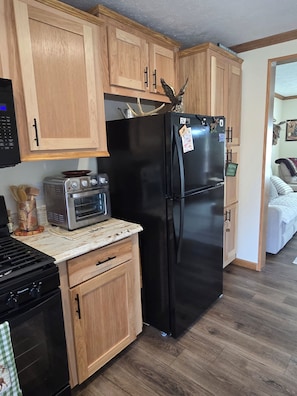 A compact kitchen with wooden cabinets, a black refrigerator, a microwave, and a stove.