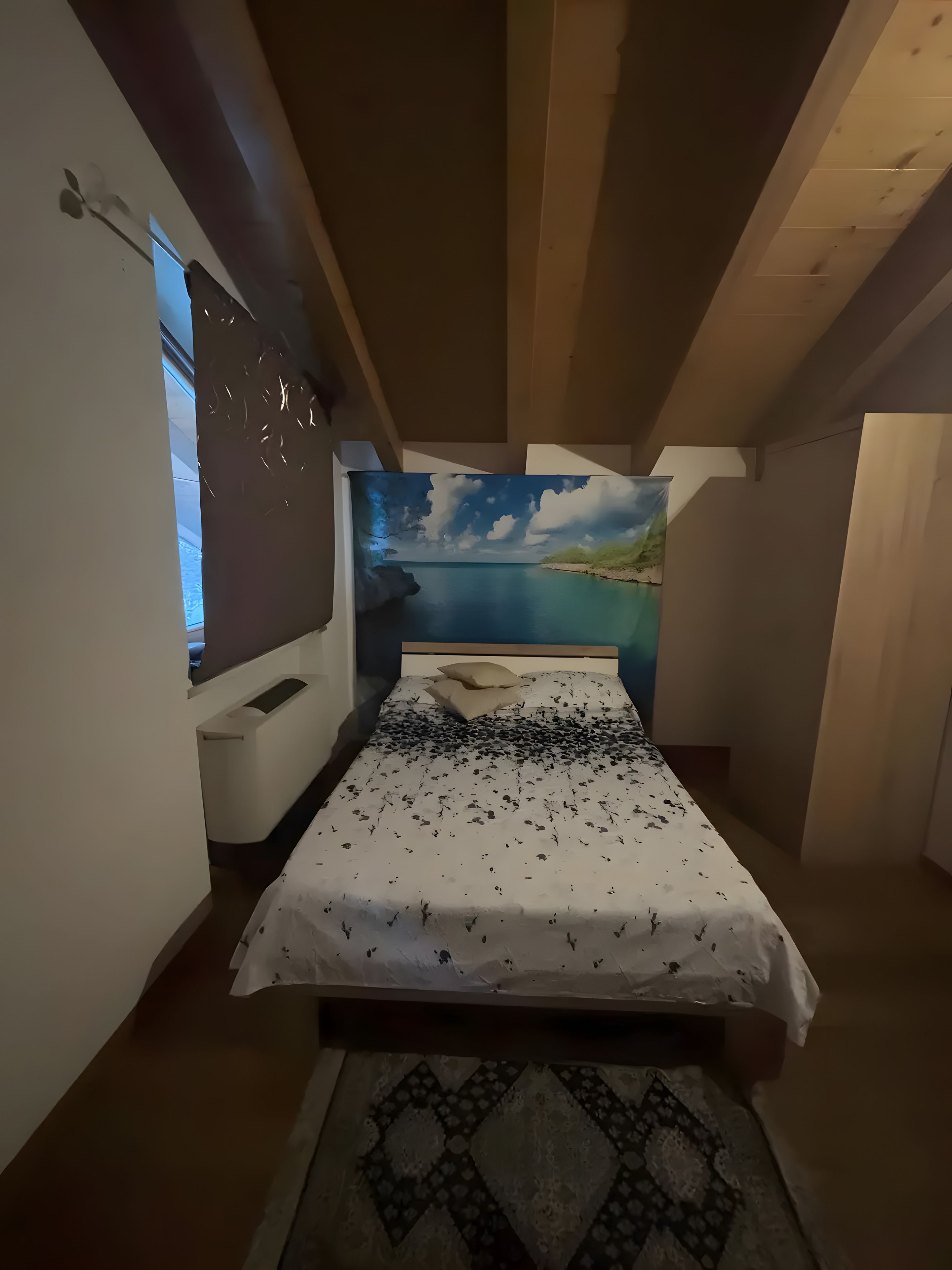 A bedroom with a bed, a nightstand, a painting of a landscape, and a window.