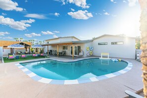 Ein Swimmingpool mit einer Fliesenkante, Liegestühlen, Sonnenschirmen und einer überdachten Terrassenanlage.
