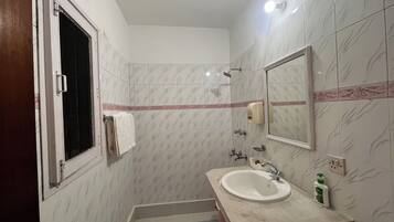 Een badkamer met een wastafel, spiegel, handdoekrek, douche en een raam.