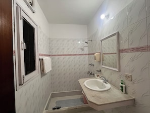 Casa de banho com lavatório, espelho, toalheiro, chuveiro e janela.