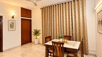 Un comedor con una mesa dispuesta para cuatro, un ventilador de techo, una planta en maceta y una puerta.