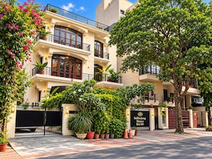 A multi-story hotel with a gated entrance, potted plants, and a sign indicating the name and address.