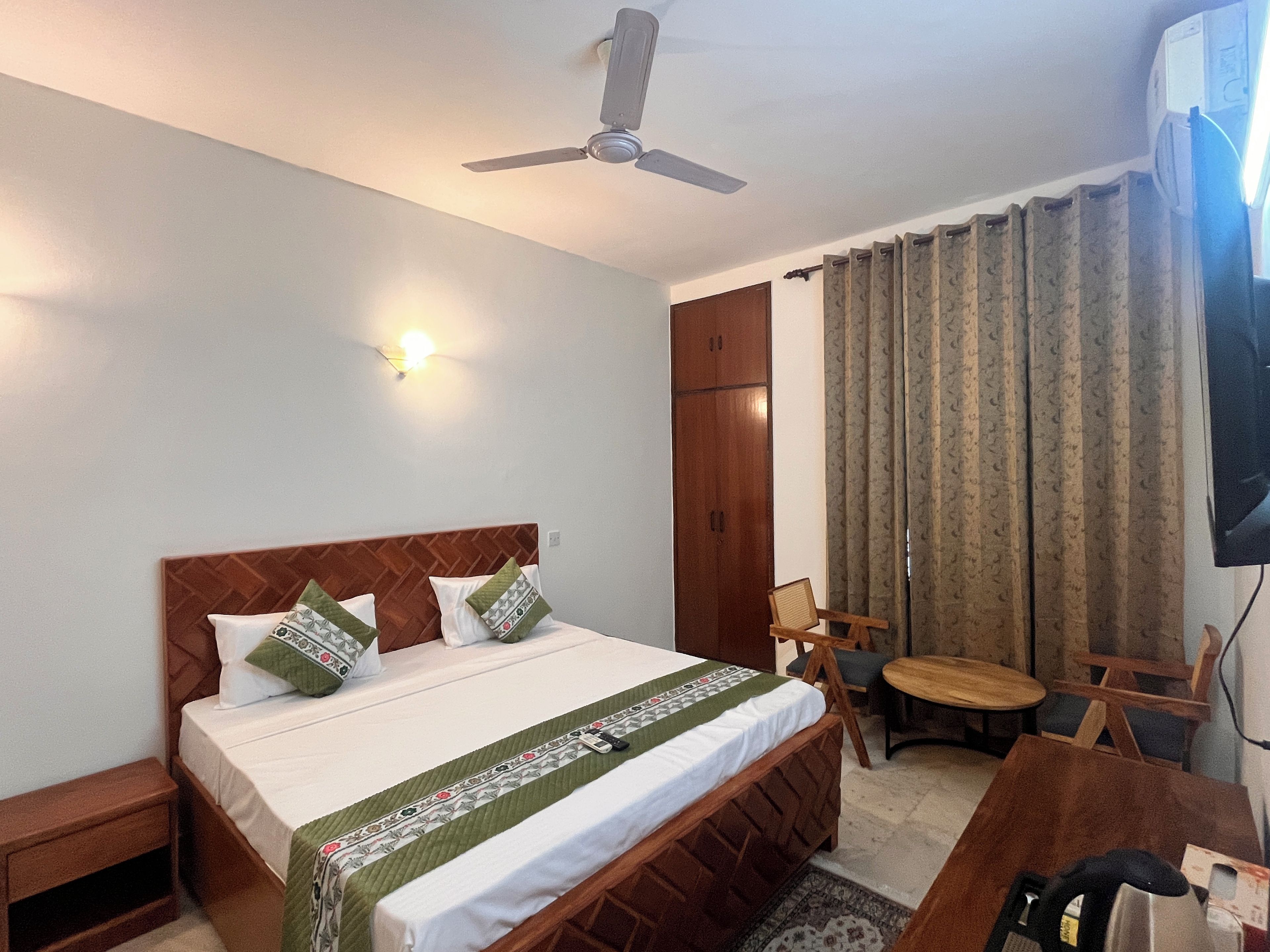 Habitación de hotel con cama, ventilador de techo, televisor, armario, escritorio y silla.
