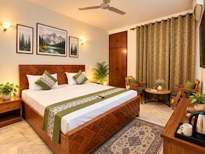 A hotel room with a bed, a desk, a chair, a small table, a plant, a ceiling fan, and curtains. - Safdarjung House (New Delhi)