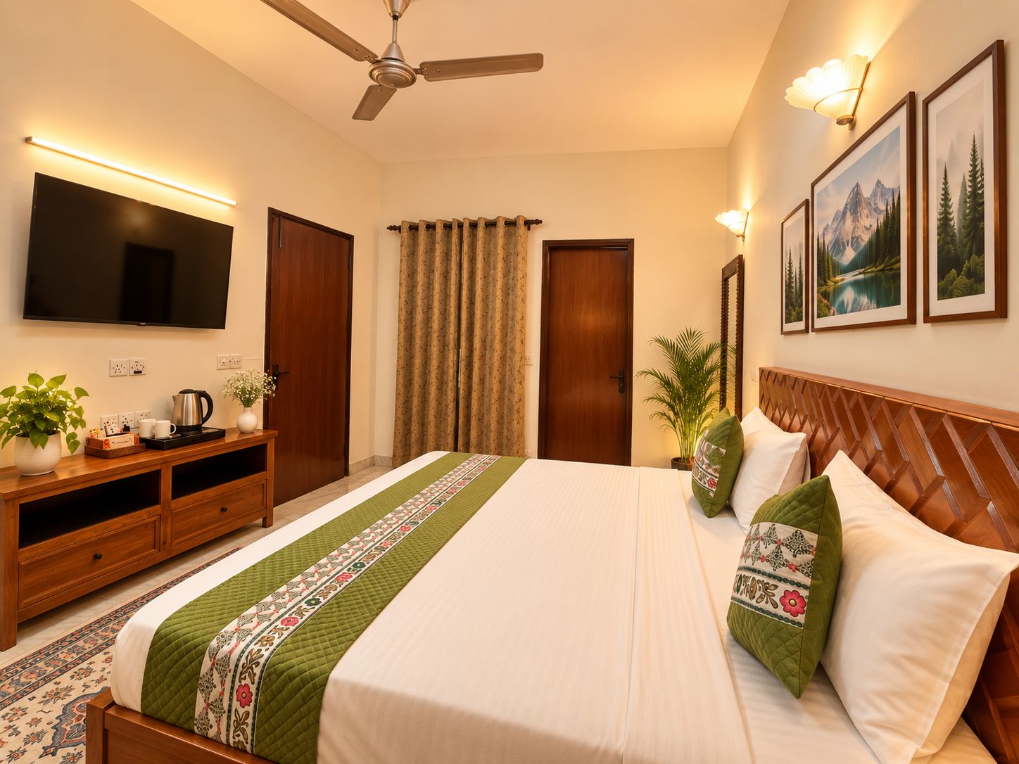 Habitación de hotel con cama, televisor de pantalla plana, ventilador de techo, cabecero de madera, mesita de noche, cafetera, planta y cuadros en la pared.