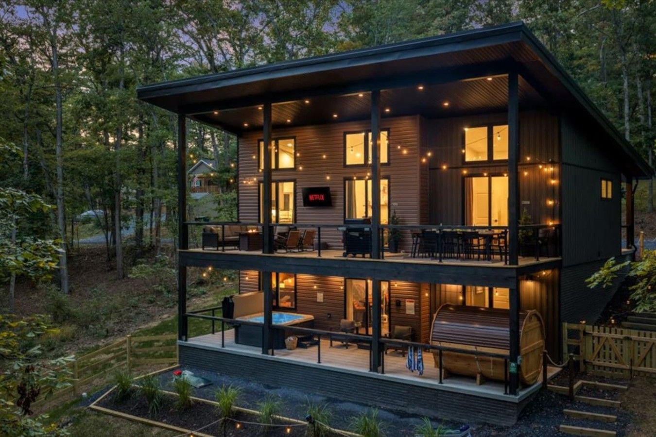 A two-story wooden cabin with a balcony, outdoor seating, and a visible Netflix logo.