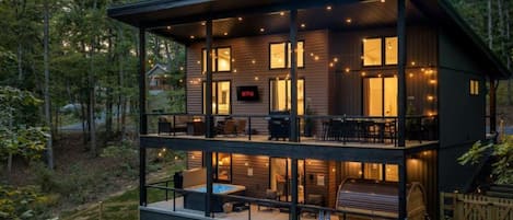 A two-story wooden cabin with a balcony, outdoor seating, and a visible Netflix logo.