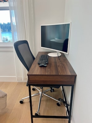 Ein Holztisch mit einem Computerarbeitsplatz, bestehend aus Monitor, Tastatur und Maus.
