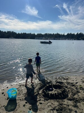 Zwei Kinder spielen nahe eines Strandes, im Hintergrund ein Boot.
