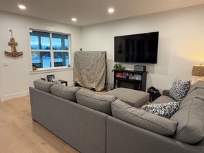 Een moderne woonkamer met een grijze modulaire bank, een flatscreen televisie aan de muur en een raam met uitzicht op een besneeerd landschap.
