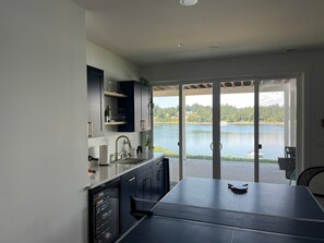 A modern kitchen with a large island, a sliding glass door leading to a lake view, and built-in cabinetry. - New Construction Luxury Waterfront Home Olympic Mtn Views & Private Beach (Bremerton)