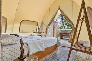A tent with a bed, a wooden swing, and a view of the outdoors.