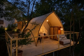 A tent with a bed and a table, surrounded by trees.